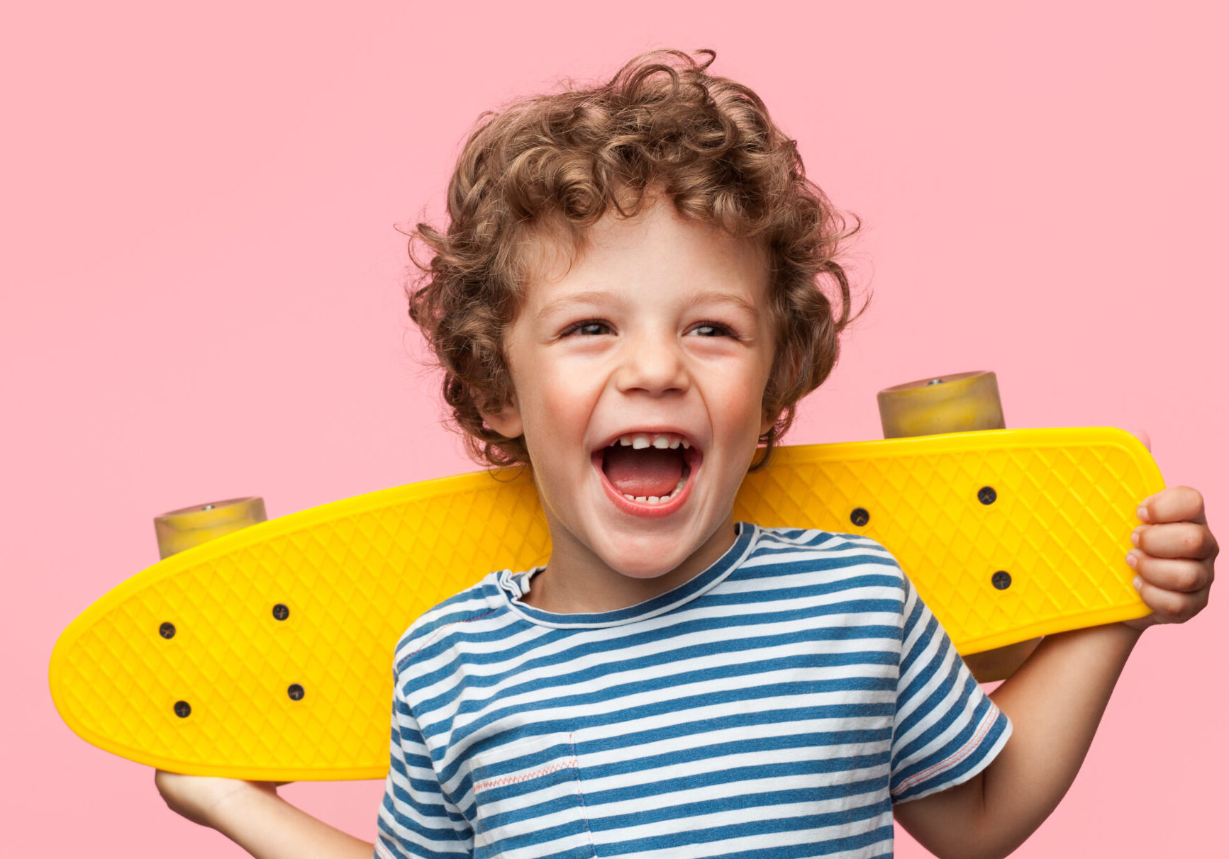 Young boy smiling holding yellow skateboard